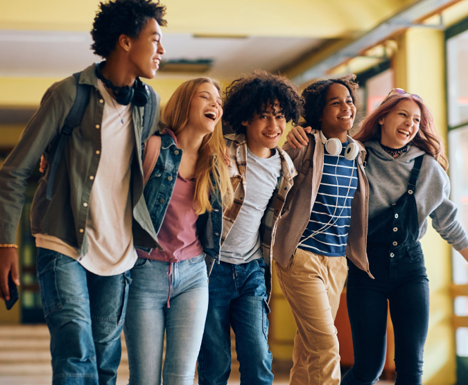 Group of teenagers walking down a hallway with arms around each other.
