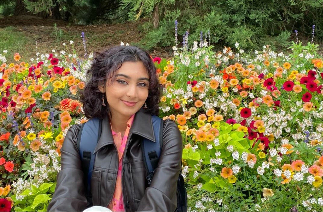 Woman sat smiling surrounded by flowers and greenery